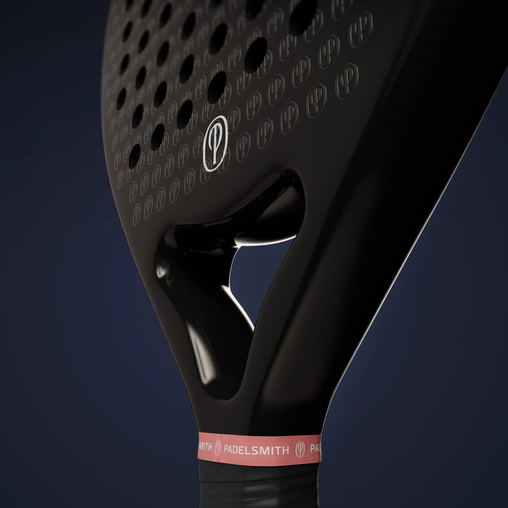 Close-up of black padel racket with perforated face, carbon texture, and pink grip band