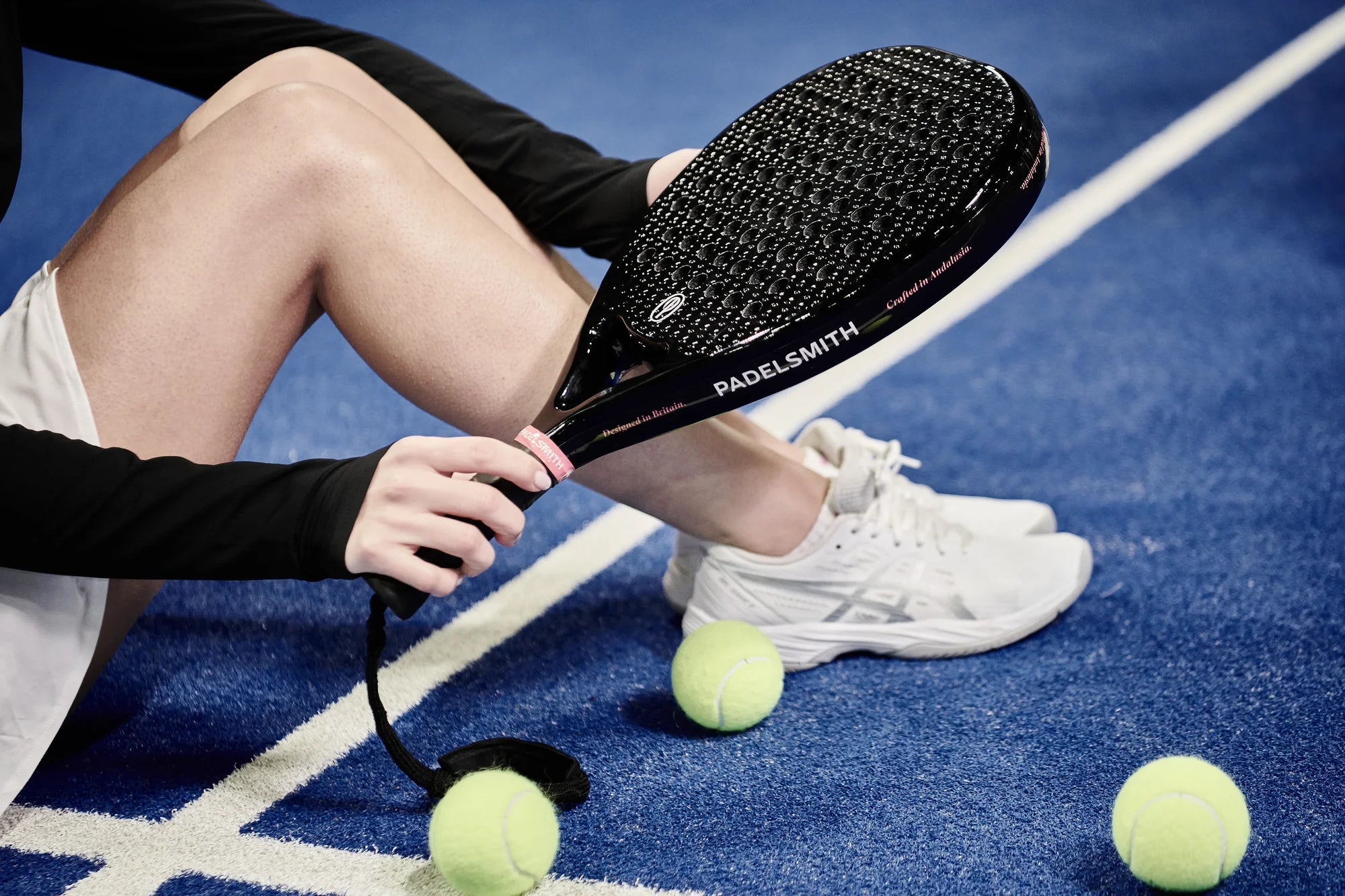Player crouching on a blue padel court holding the Padelsmith #1 racket with yellow padel balls beside them