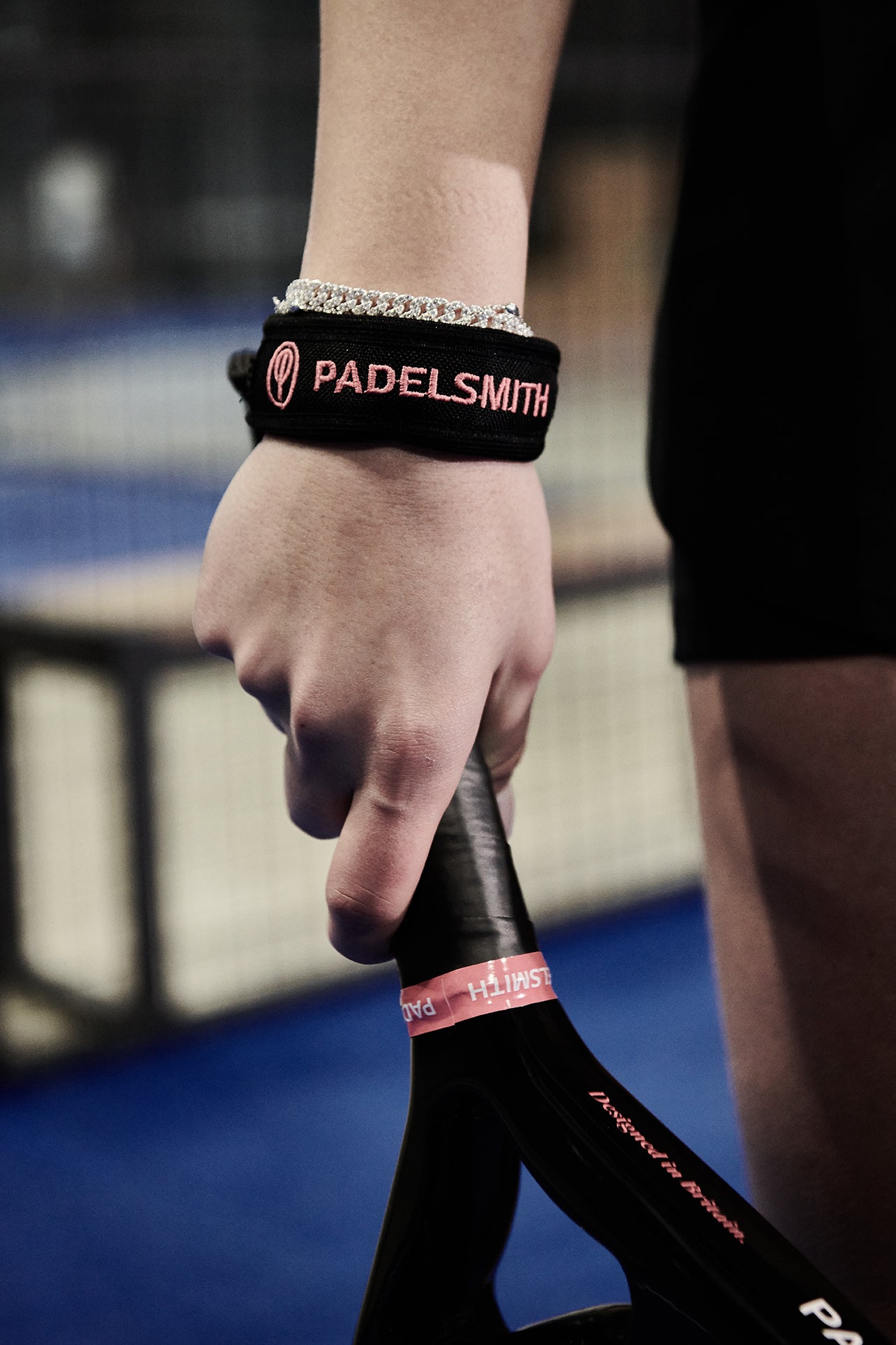 Hand wearing a PADELSMITH wristband holding a paddle on a blurred background