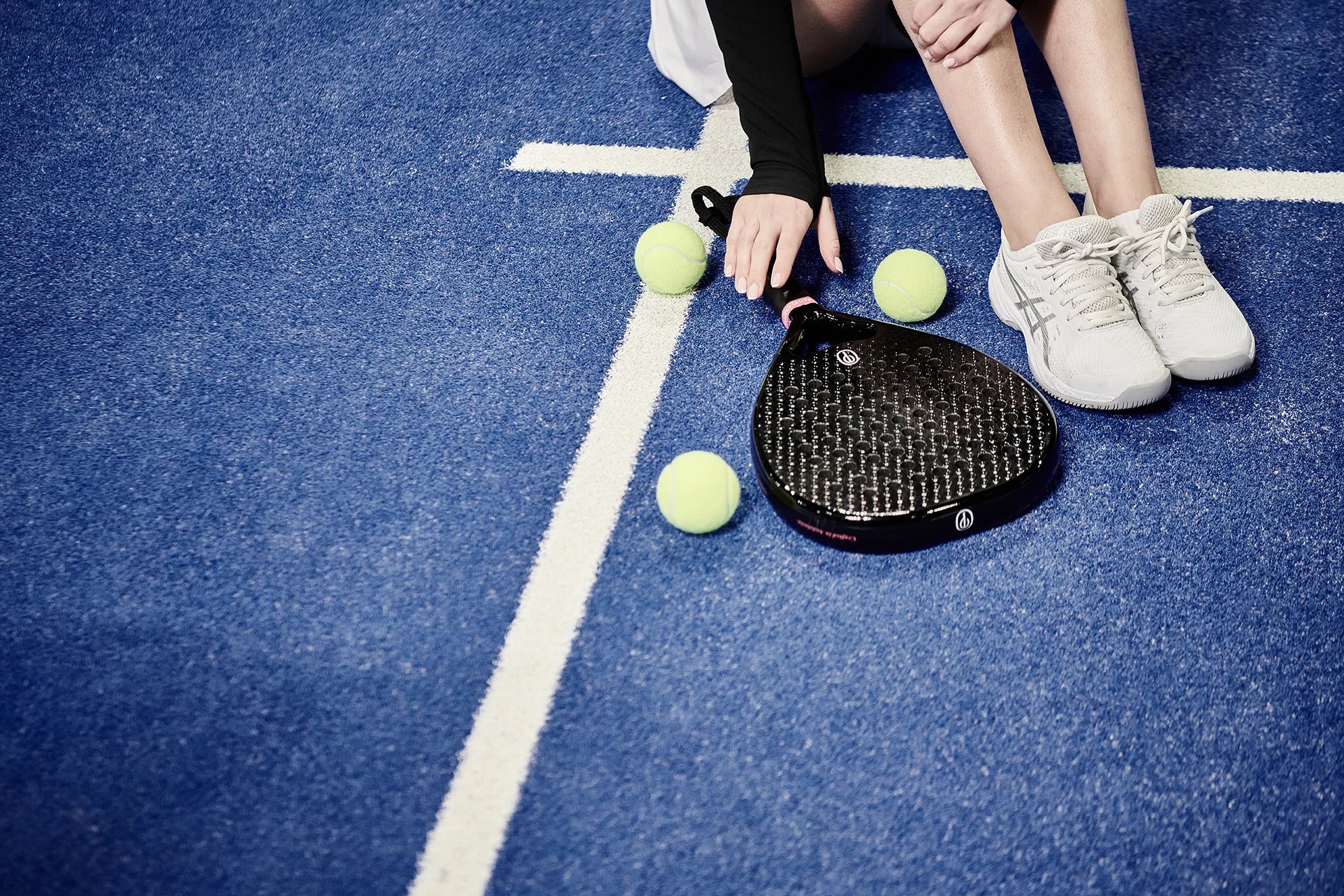 Padelsmith #1 padel racket beside three yellow padel balls and a player's trainers on a blue padel court
