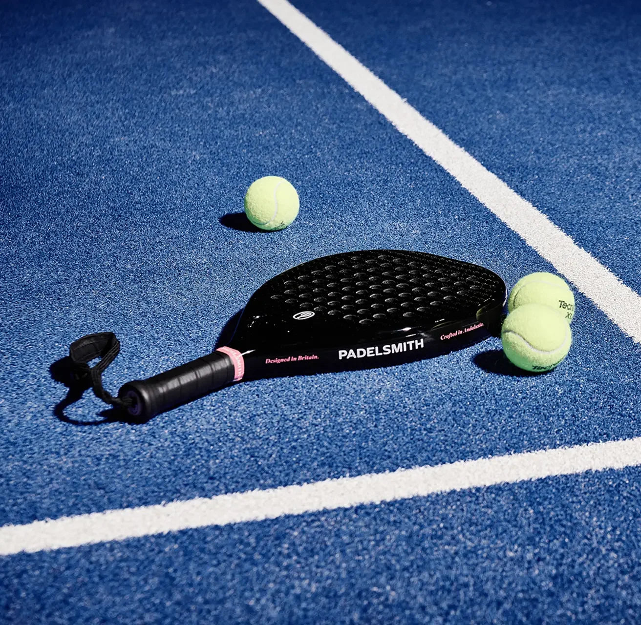 Black padel racket and yellow balls on blue outdoor court with white lines