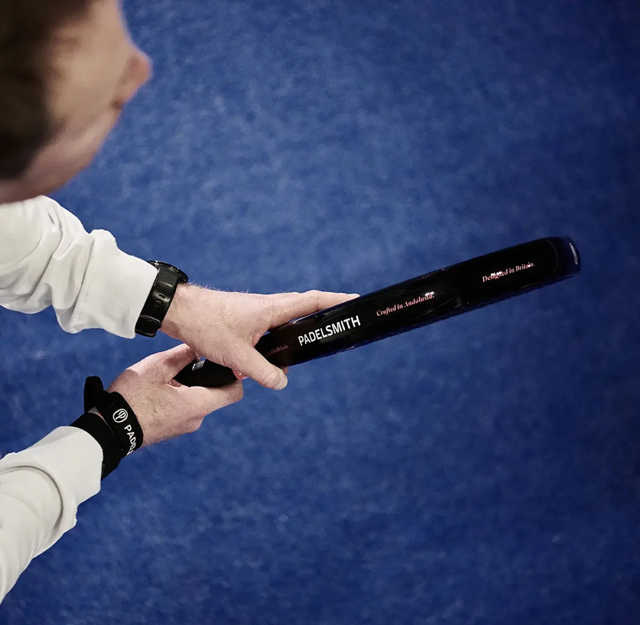 Person holding a premium padel racket with visible branding on a blue court.
